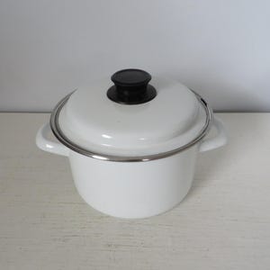 May include: A white enamel pot with a matching lid and a black handle. The pot has two side handles and a silver rim. This kitchenware is suitable for cooking.