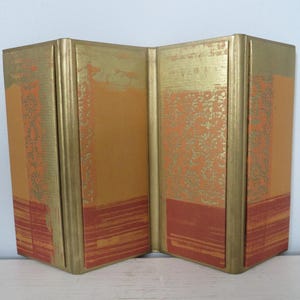 May include: A four-panel room divider made of wood with a gold and orange patterned design. The panels are hinged together and can be folded up for storage.