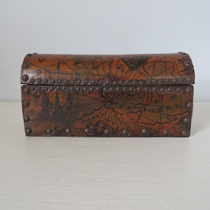 May include: A small, rectangular wooden chest with a curved lid. The chest is brown with a map design and metal studs. The map design features ships and nautical elements. A decorative storage box.