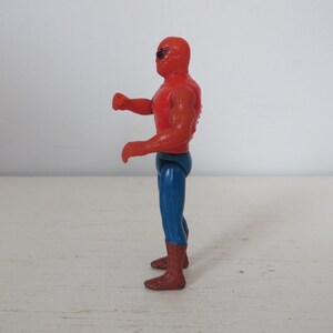 May include: A red and blue plastic action figure of a superhero wearing a mask. The figure is posed with one arm raised and the other bent at the elbow.