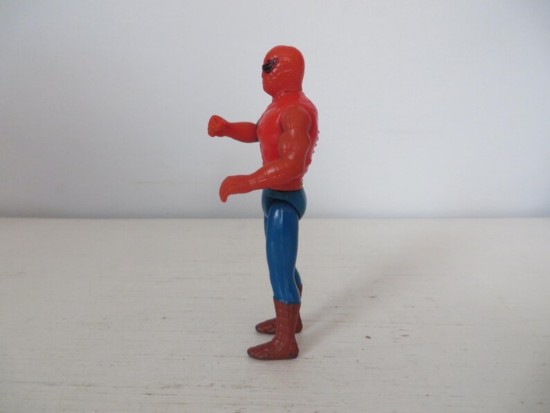 May include: A red and blue plastic action figure of a superhero wearing a mask. The figure is posed with one arm raised and the other bent at the elbow.