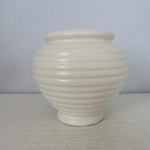 May include: A white ceramic vase with a ribbed design. The vase is round and has a wide opening.