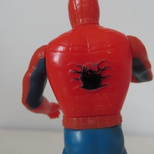 May include: Red and blue plastic action figure of Spider-Man with a black spider symbol on the back. The figure has the text "MARVEL C. 1973 HONG KONG" printed on the back.
