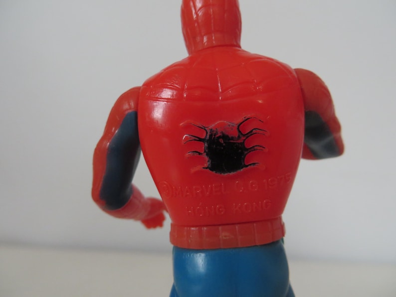 May include: Red and blue plastic action figure of Spider-Man with a black spider symbol on the back. The figure has the text "MARVEL C. 1973 HONG KONG" printed on the back.