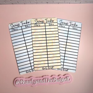 May include: Three rectangular savings tracker cards with black grid lines, headers for Category and Balance, and the text Savings Tracker. The center card features a yellow honeycomb pattern, while the outer cards have blue and white gradients. The text Beauty and the Budgett appears at the bottom of each card and on a separate pink sign.