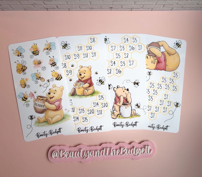 May include: Four white rectangular savings challenge sheets featuring Winnie the Pooh illustrations, honey pots, bees, and honeycomb patterns with dollar amounts. Each sheet includes the text Beauty and the Budget and a separate pink sign with the text @BeautyandtheBudget.