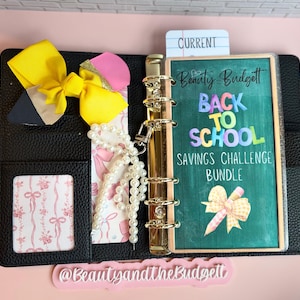 Puede incluir: Una carpeta de textura de cuero negro con un mecanismo de seis anillas doradas, un lazo amarillo y un dije de cuentas de perlas blancas. La portada muestra el texto Beauty Budgett BACK TO SCHOOL SAVINGS CHALLENGE BUNDLE con un gráfico de lápiz.