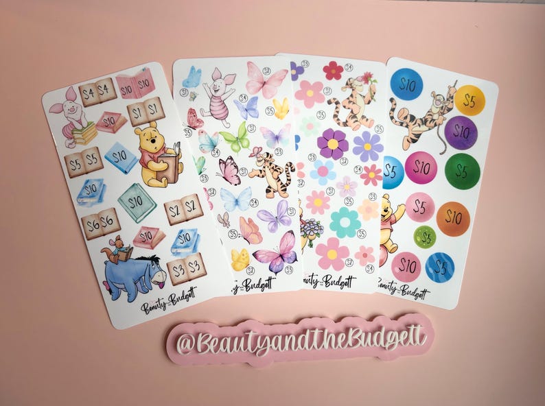 May include: Four rectangular sticker sheets featuring Winnie the Pooh characters, butterflies, flowers, and numbered circles with dollar amounts. Each sheet includes the text Beauty and the Budget. A pink sign displays @BeautyandtheBudgett.