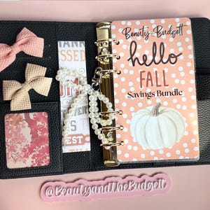 Puede incluir: Una carpeta negra texturizada con una cubierta color melocotón con lunares blancos, una ilustración de calabaza blanca y el texto Beauty Budget hello FALL Savings Bundle. Incluye dos lazos de tela pequeños, un dije de perlas y un inserto floral.