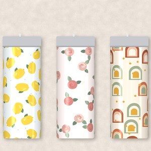 May include: Three cylindrical tumblers with distinct patterns. The first features yellow lemons and green leaves on white. The second displays pink roses with green leaves on white. The third shows a repeating pattern of arches in terracotta, sage green, and yellow.