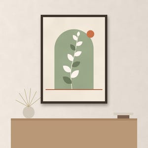 May include: A framed wall art print featuring a sage green arch shape containing a white leafy plant stem. A small burnt orange circle sits in the upper right corner of the arch, and a thin horizontal red line runs across the bottom of the frame.