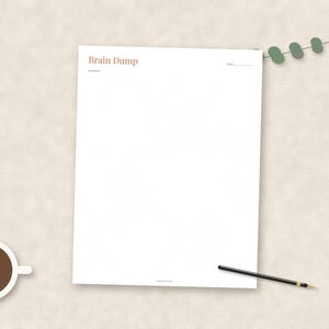 May include: A white paper sheet with a grid pattern and the text Brain Dump printed in brown at the top left corner. The sheet includes a date line in the top right corner. A black pen and a cup of coffee are positioned near the paper.
