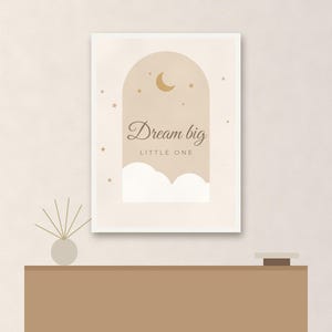 May include: A rectangular wall print featuring an arched window design in shades of beige and cream. The artwork displays a crescent moon, small stars, and white clouds with the text Dream big LITTLE ONE centered in dark brown script and print.