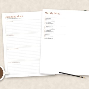 May include: Two white paper planners with black text and terracotta headings. One sheet is titled Dopamine Menu with sections for 5 minutes, 30 minutes, and longer tasks. The other is a Weekly Reset checklist with home, life, and me categories.
