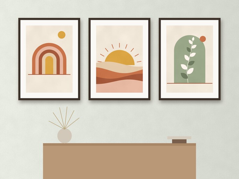 May include: Three framed wall art prints featuring abstract designs. The left print shows a rainbow and sun, the center print depicts a sun over layered hills, and the right print displays a green arch with a white leaf branch and a small red circle.