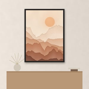 May include: A framed wall art print featuring a layered mountain landscape in shades of beige, tan, and brown with a solid circular sun. The artwork is displayed above a flat-topped console table with a small reed diffuser and a square object.