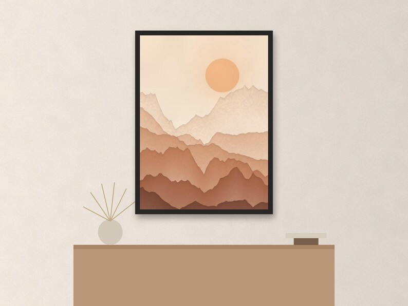 May include: A framed wall art print featuring a layered mountain landscape in shades of beige, tan, and brown with a solid circular sun. The artwork is displayed above a flat-topped console table with a small reed diffuser and a square object.