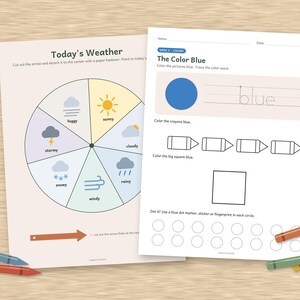 May include: Two educational worksheets on a wooden surface. The left sheet features a circular weather chart titled Today's Weather with icons for sunny, cloudy, rainy, windy, snowy, stormy, and foggy conditions. The right sheet is titled The Color Blue.