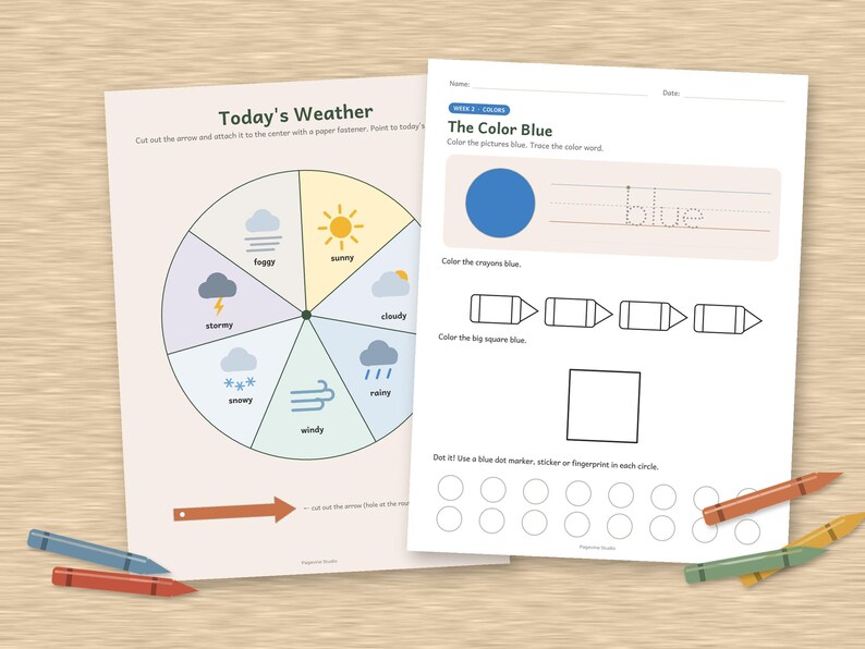 May include: Two educational worksheets on a wooden surface. The left sheet features a circular weather chart titled Today's Weather with icons for sunny, cloudy, rainy, windy, snowy, stormy, and foggy conditions. The right sheet is titled The Color Blue.