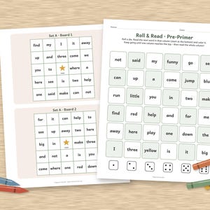 May include: Educational worksheets featuring Roll & Read Pre-Primer word grids with columns of sight words and dice icons at the bottom. Two smaller boards labelled Set A Board 1 and 2 are included, with colourful crayons placed around the pages.