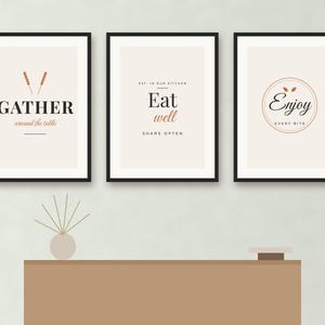 May include: Three framed wall art prints with black frames and cream backgrounds. The first print says GATHER around the table with wheat stalks. The second says Eat well SHARE OFTEN. The third says Enjoy EVERY BITE inside a circular border.