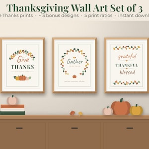 May include: A set of three framed wall art prints featuring Thanksgiving themes. The prints display the text Give THANKS, Gather TOGETHER, and grateful THANKFUL blessed, decorated with autumn-coloured leaf wreaths and small pumpkin illustrations.