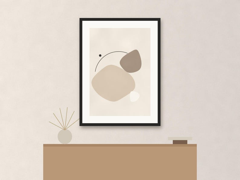May include: A framed wall art print featuring an abstract composition of organic shapes in shades of beige, taupe, and white, accented by a thin black curved line and a small black dot, all enclosed within a simple black rectangular frame.