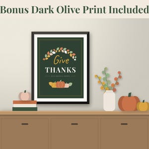 May include: A framed wall art print featuring a dark green background with the text Give THANKS with grateful hearts. The design includes a colourful autumn leaf wreath at the top and a row of pumpkins at the bottom. Text reads Bonus Dark Olive Print Included.