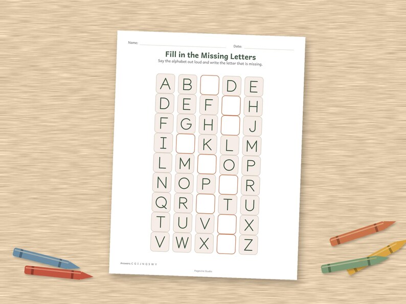 May include: A white educational worksheet titled Fill in the Missing Letters with a grid of alphabet letters in black ink. The page features empty boxes for students to complete the sequence. Several colored crayons are scattered around the paper.