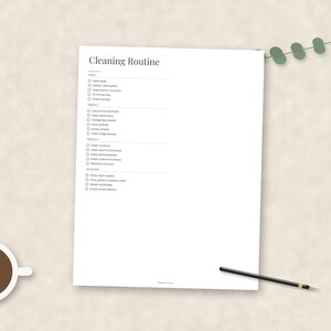 May include: A white paper cleaning routine checklist with black text organized into daily, weekly, monthly, and seasonal sections. The document features checkboxes for each task, a cup of black coffee, and a black pen placed on the page.