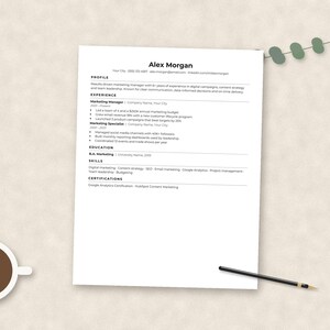 May include: A white resume document titled Alex Morgan with sections for profile, experience, education, skills, and certifications. The document is accompanied by a cup of dark coffee and a thin black pen, arranged on a neutral textured surface.