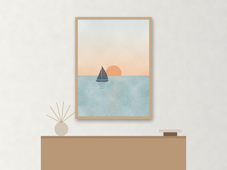 May include: A framed vertical wall art print featuring a dark blue sailboat on a textured light blue sea under a soft peach sky with a round orange sun. The artwork is displayed in a light wood frame, capturing a serene nautical scene.