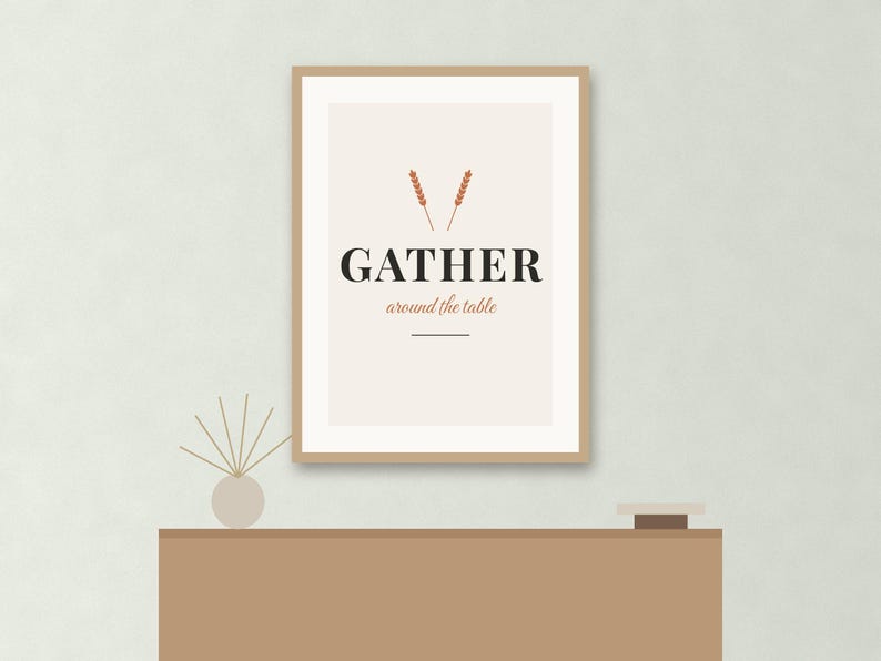 May include: A framed wall art print with a light beige background featuring two small orange wheat stalks above the black text GATHER and the smaller orange text around the table, with a horizontal line underneath the text.