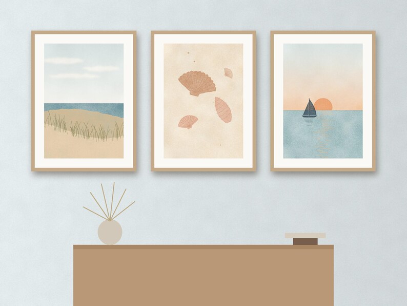 May include: Three framed wall art prints featuring coastal scenes. The left print shows a beach with dunes and grass. The center print displays various seashells on a beige background. The right print depicts a sailboat on water at sunset.