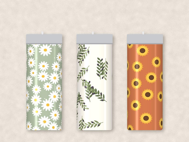 May include: Three cylindrical tumblers with flat gray lids. The left tumbler features a sage green background with white daisy patterns. The center tumbler has a cream background with green olive branch motifs. The right tumbler displays sunflowers.