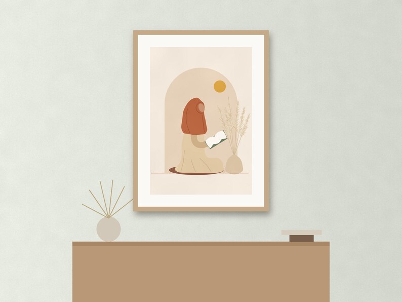 May include: A framed wall art print featuring a stylized illustration of a person wearing a rust-colored head covering and a beige garment, sitting and reading a book. The scene includes a yellow sun, an arched doorway, and a vase with dried grass.