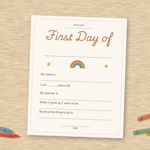 May include: A white paper sheet with the text First Day of school year, featuring a small rainbow and two stars. The form includes blank lines for name, age, teacher, future career, favorite activity, and date, surrounded by scattered colored crayons.