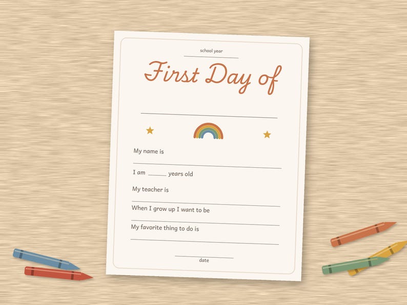 May include: A white paper sheet with the text First Day of school year, featuring a small rainbow and two stars. The form includes blank lines for name, age, teacher, future career, favorite activity, and date, surrounded by scattered colored crayons.