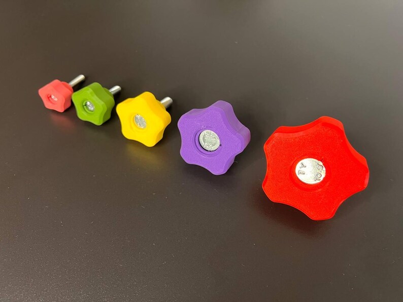 Peut inclure: Un ensemble de cinq boutons en forme d'&eacute;toile de tailles gradu&eacute;es, comprenant un rouge, un vert, un jaune, un violet et un plus grand rouge. Chaque bouton poss&egrave;de un boulon m&eacute;tallique central avec une tige filet&eacute;e d&eacute;passant &agrave; l'arri&egrave;re.