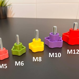 May include: A set of five star-shaped knobs with threaded metal studs, arranged by size and color. The knobs are labeled M5, M6, M8, M10, and M12. The colors include red, green, yellow, purple, and a larger red knob, each featuring a central metal bolt.