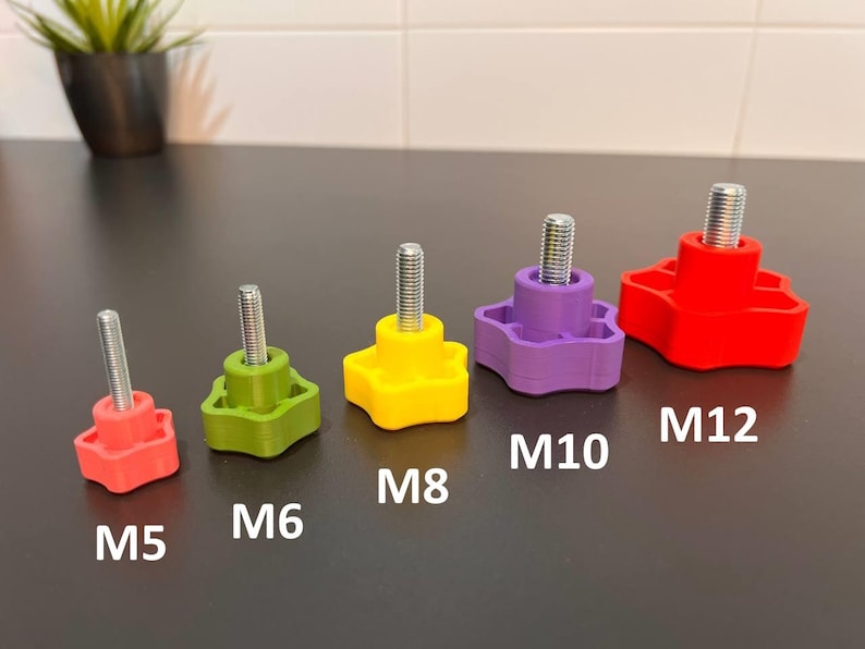 Peut inclure: Un ensemble de cinq boutons en forme d'&eacute;toile avec des tiges filet&eacute;es en m&eacute;tal, dispos&eacute;s par taille et couleur. Les boutons sont &eacute;tiquet&eacute;s M5, M6, M8, M10 et M12. Les couleurs incluent rouge, vert, jaune, violet et un bouton rouge plus grand.