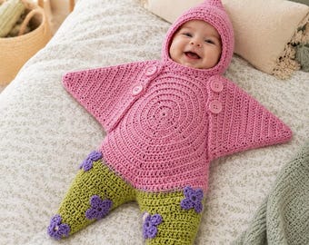 Könnte beinhalten: Ein gehäkelter, sternförmiger Babyschlafsack in Rosa und Grün mit Kapuze. Der obere Teil ist rosa mit vier passenden Knöpfen, während der untere Teil grün ist und mit violetten, gehäkelten Blumenapplikationen an den Beinen versehen ist.
