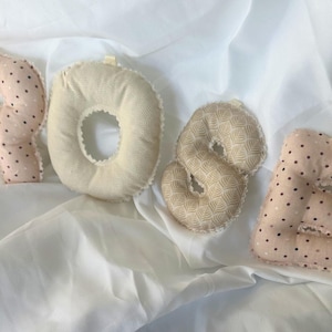 Può includere: Quattro lettere di stoffa che compongono la parola "ROSE" sono esposte su un tessuto bianco. La lettera "R" è rosa chiaro con pois marrone scuro. La "O" è color crema. La "S" è beige chiaro con un motivo geometrico. La "E" è rosa chiaro con pois marrone scuro.