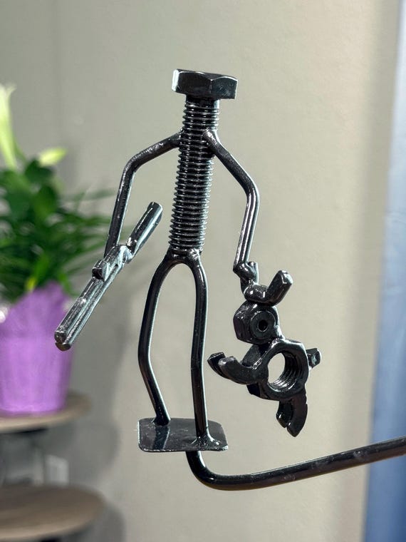 A kinetic desk sculpture made from welded bolts and hardware depicting a hunter with his dog — legitimately handcrafted industrial folk art with real personality.