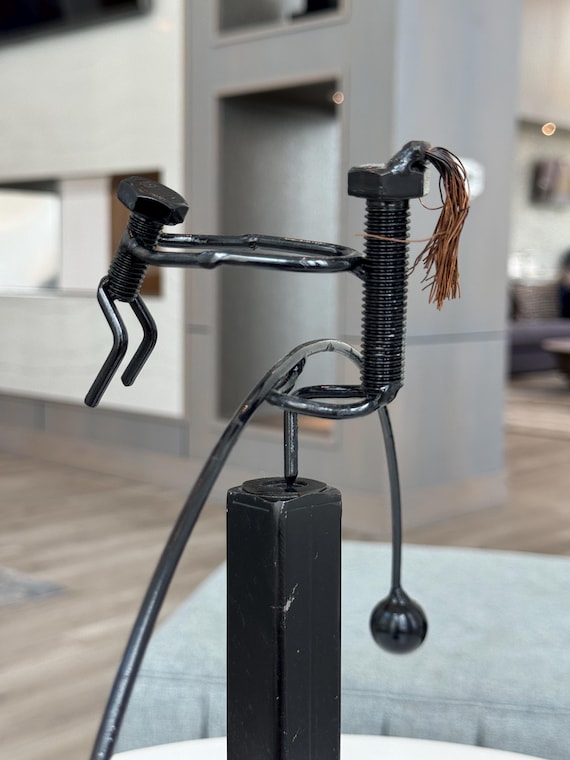 A hand-crafted metal kinetic sculpture where a mother and child figure balance and sway in mesmerizing motion — actual moving desk art that feels alive.
