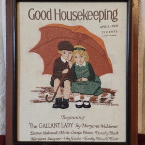 May include: A framed embroidery depicting a 1926 Good Housekeeping magazine cover. It features two children under an orange umbrella, with text including "Good Housekeeping," "April 1926," "25 Cents," and "Beginning The Gallant Lady" by Margaret Widdemer.