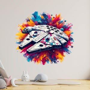 Könnte beinhalten: Illustration des Raumschiffs Millennium Falcon in Weiß und Grau mit farbenfrohen Farbspritzern. Das Raumschiff hat ein detailliertes Design mit mehreren kreisförmigen Fenstern und einem zentralen Cockpit. Der Hintergrund zeigt lebendige Spritzer in Gelb, Orange, Blau und Pink.