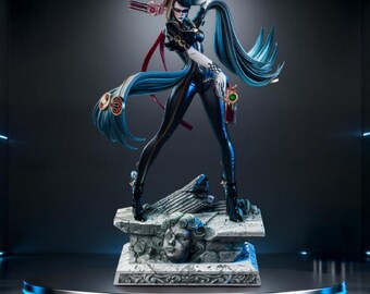 May include: A detailed statue of a female character in a dynamic pose, wearing a black bodysuit with long, flowing blue hair. She holds two pistols and stands on a stone base with a sculpted face. The statue is on a round, illuminated platform.