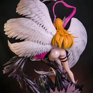 May include: A detailed figurine of a woman with long, flowing blonde hair, wearing a white and black outfit, and large white feathered wings. The figure is posed with a pink heart-shaped accent and stands on a dark, textured base with crystal-like elements.