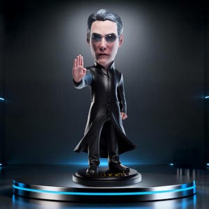 May include: A bobblehead figurine of a character from The Matrix. The figure is wearing a long black coat and sunglasses, with a hand raised in a stopping gesture. The base is black with gold lettering, and the figure stands on a round platform.